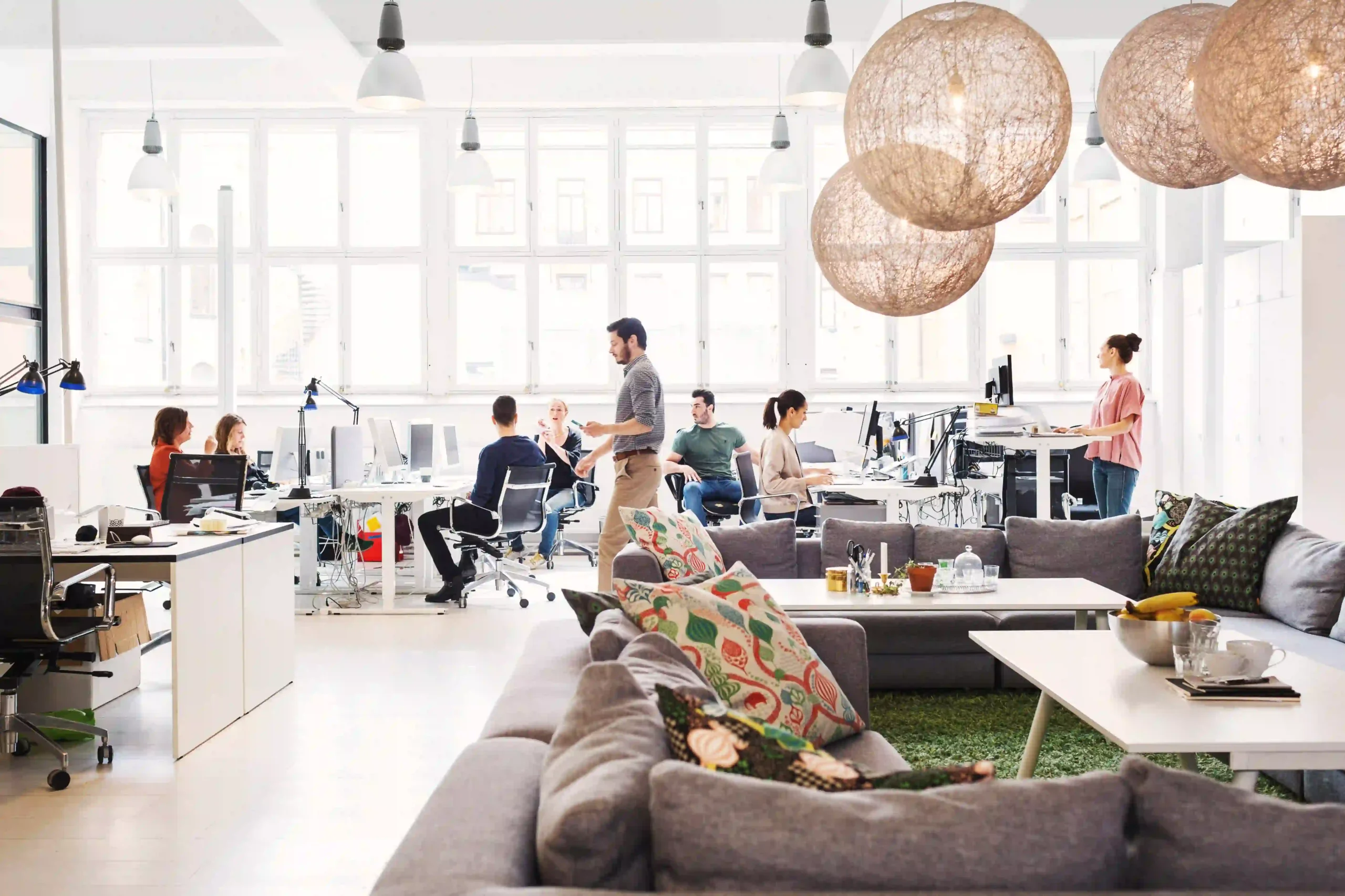 Bright, cozy office interior with staff augmentation team members working and collaborating at computer workstations with sofas and desks.