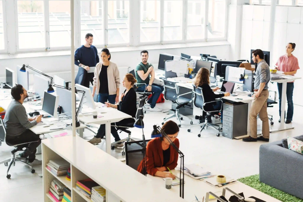 Busy open-plan office with multiple staff augmentation developers working at desks and collaborating in groups.